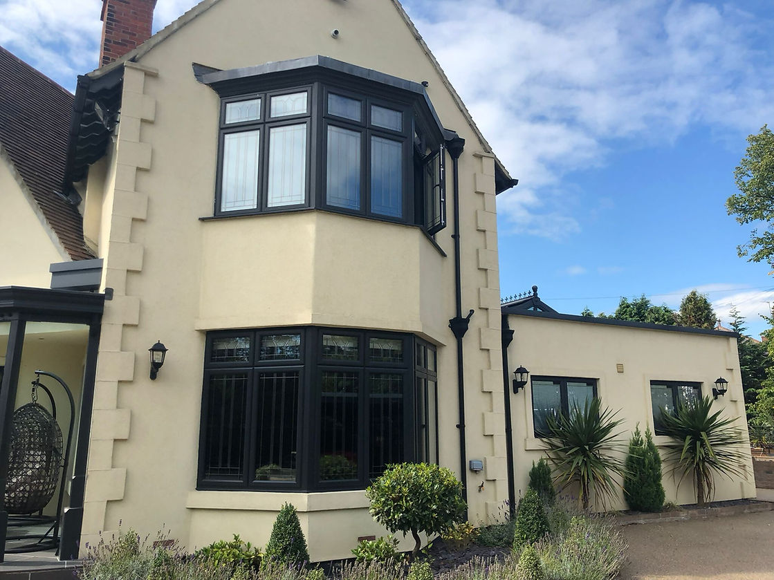 Two-story cream house with black trim, angular bay windows, and a sloped roof