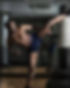 A muscular man kicking a punching bag.