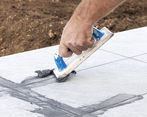 Hand using a grout float to apply mortar between large floor tiles