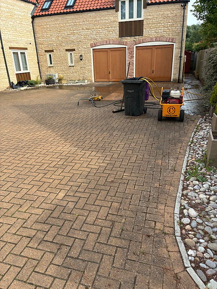 Residential brick paver driveway partially pressure washed, showing clean and dirty sections