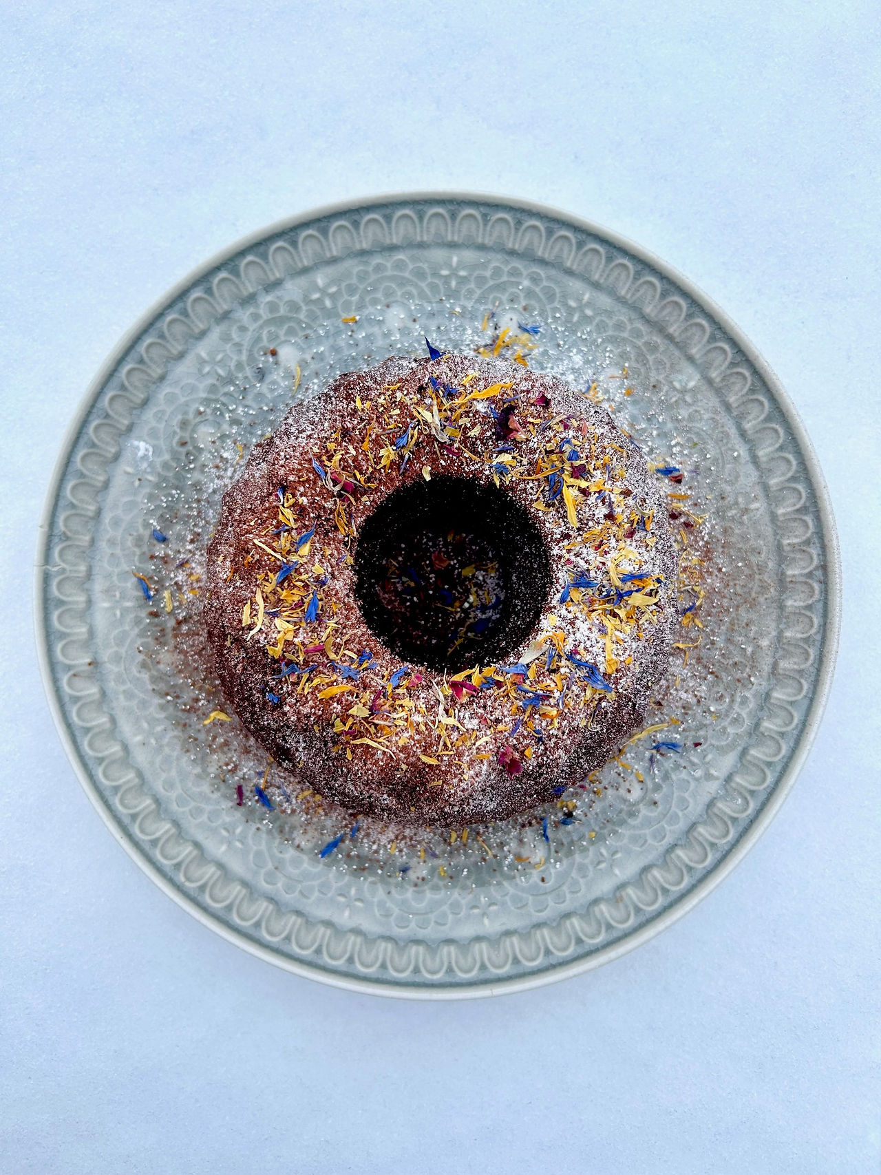 Veganer Brownie-Gugelhupf aus kleiner Gugelhupfform, von oben fotografiert, saftiger Schokokuchen mit Puderzucker, Kakao und essbaren Blüten dekoriert