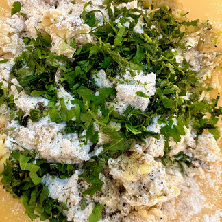 Geriebene Kartoffeln und Zucchini vermengt mit frischen gehackten Kräutern, Mehl und Gewürzen in einer großen gelben Schüssel – Basis für die Zubereitung der Zucchini-Kartoffelpuffer.