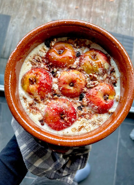 Ungebackene vegane Bratäpfel in einer Auflaufform mit cremiger Vanillesauce, Nüssen und Rosinen. Vorbereitung eines winterlichen Desserts – saftig, aromatisch und pflanzlich.