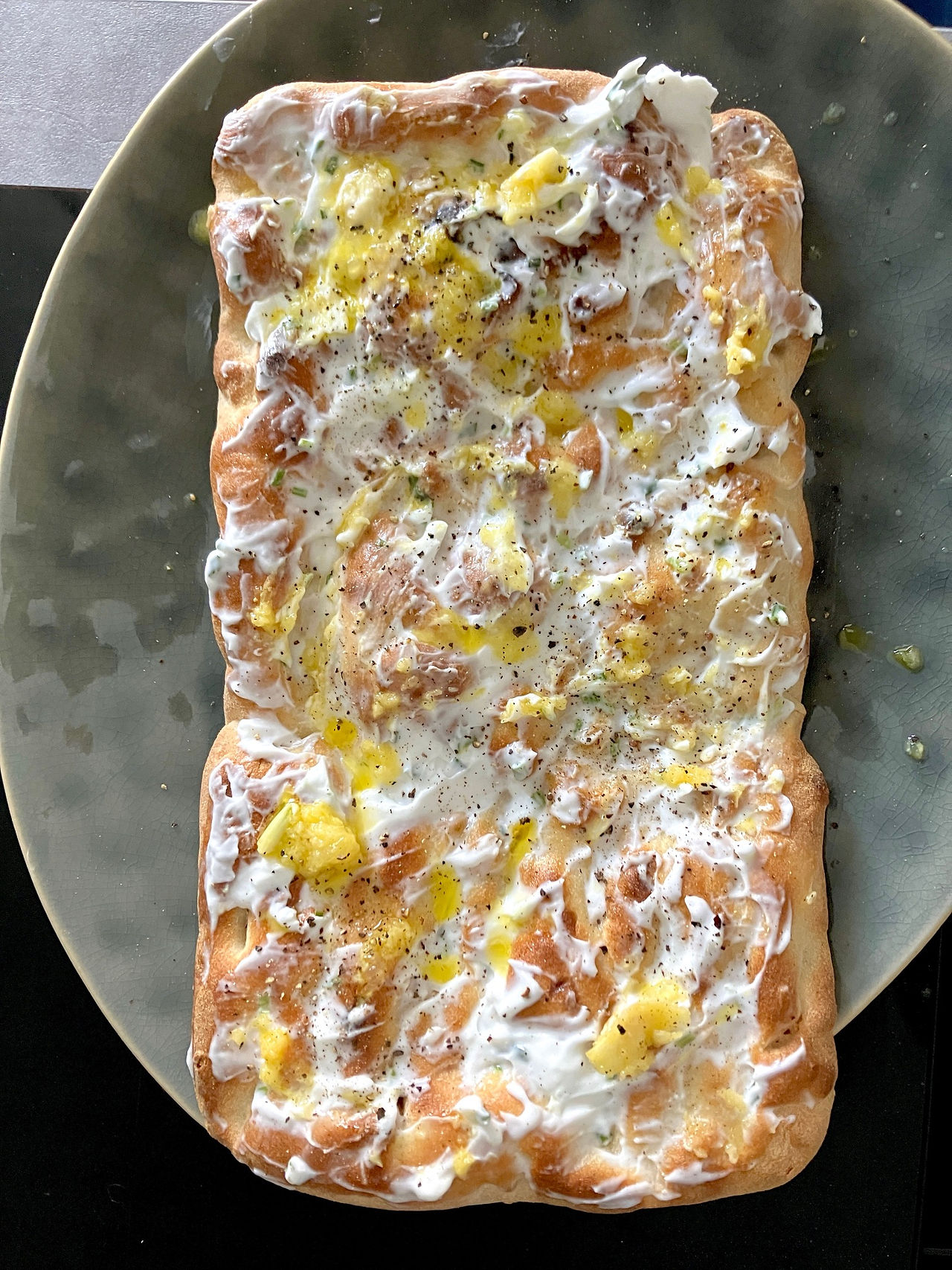 Erster Schritt beim Belegen der veganen Portobello-Pinsa: knuspriger Holzofenboden bestrichen mit Zitronen-Knoblauch-Creme aus veganem Frischkäse, Rapsöl und frischem Pfeffer.