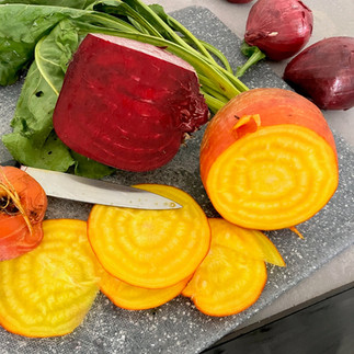 Frisch angeschnittene rote und gelbe Bete mit intensivem Farbmuster, daneben rote Zwiebeln auf einer grauen Arbeitsplatte – die gelbe Bete zeigt ihre typische Ringelstruktur.