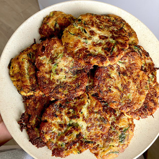 Mehrere frisch gebratene, goldbraune Zucchini-Kartoffelpuffer auf einem hellen, runden Teller – angerichtet in einer leicht überlappenden Schichtung, bereit zum Servieren.