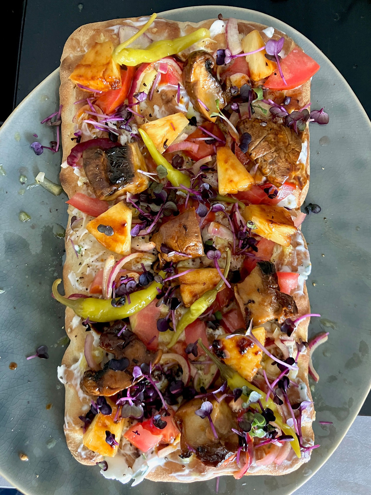 Fertig belegte vegane Portobello-Pinsa mit gebratenem Pilz, Ananas, Tomaten, eingelegten Zwiebeln, scharfen Peperoni und frischer Rettichkresse – servierbereit und bunt angerichtet.