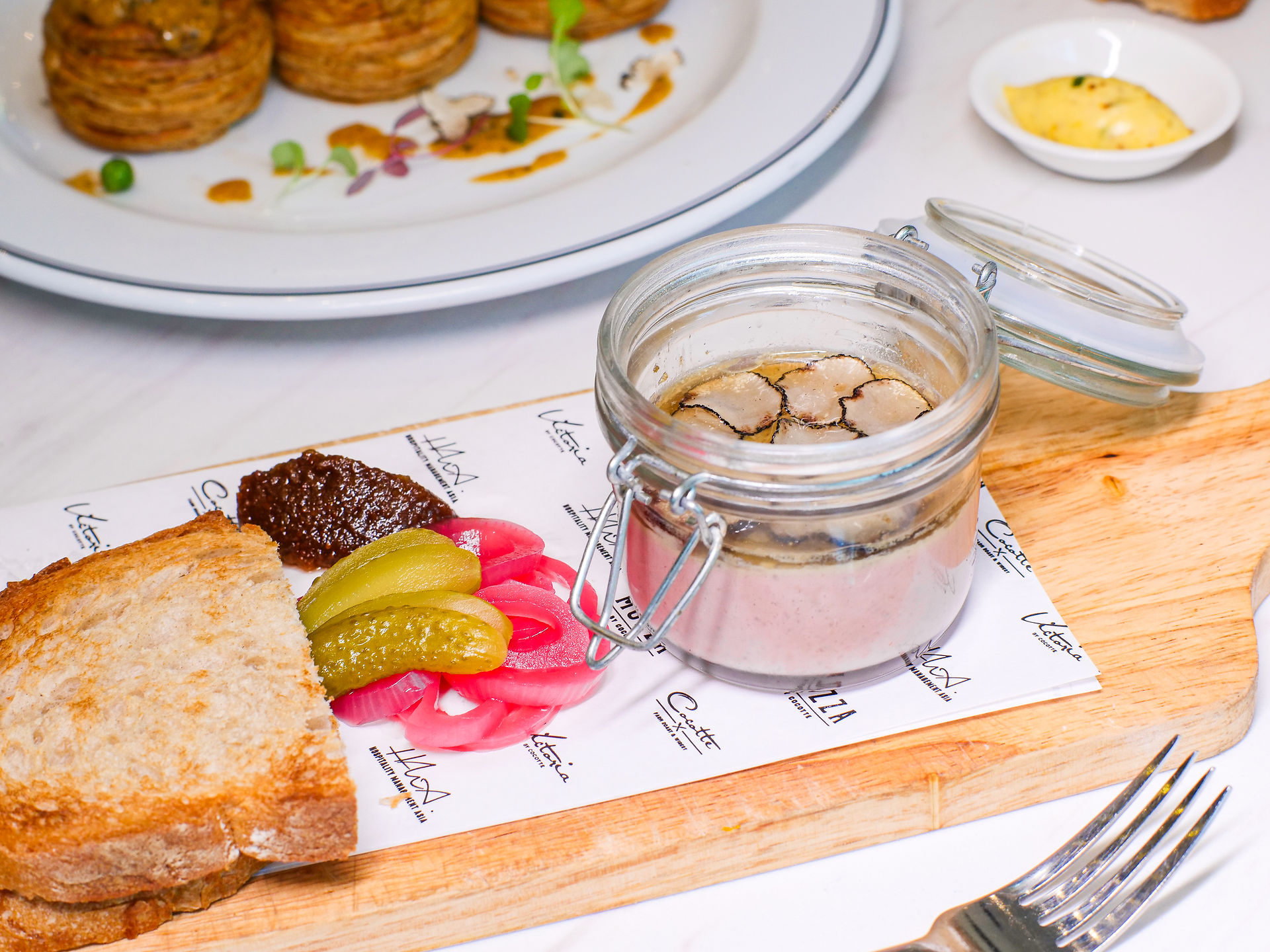 Truffle Liver paté on a wooden board, decorated with toasted bread, gherkin and pickled shallots