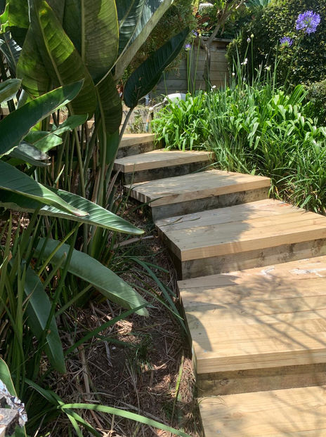 A wide shot showcasing a wooden pine sleeper pathway winding through the garden, blending seamlessly with the landscape