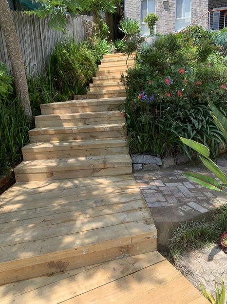 A wide shot showcasing a wooden pine sleeper pathway winding through the garden, blending seamlessly with the landscape