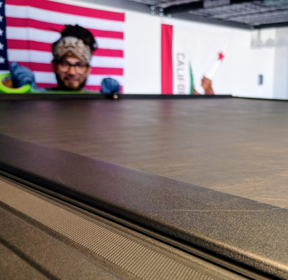 "Close-up, low-angle view of a freshly cleaned tonneau cover on a black Chevrolet Silverado High Country, with a 274CarWashOnTheSpot.com technician in the background."