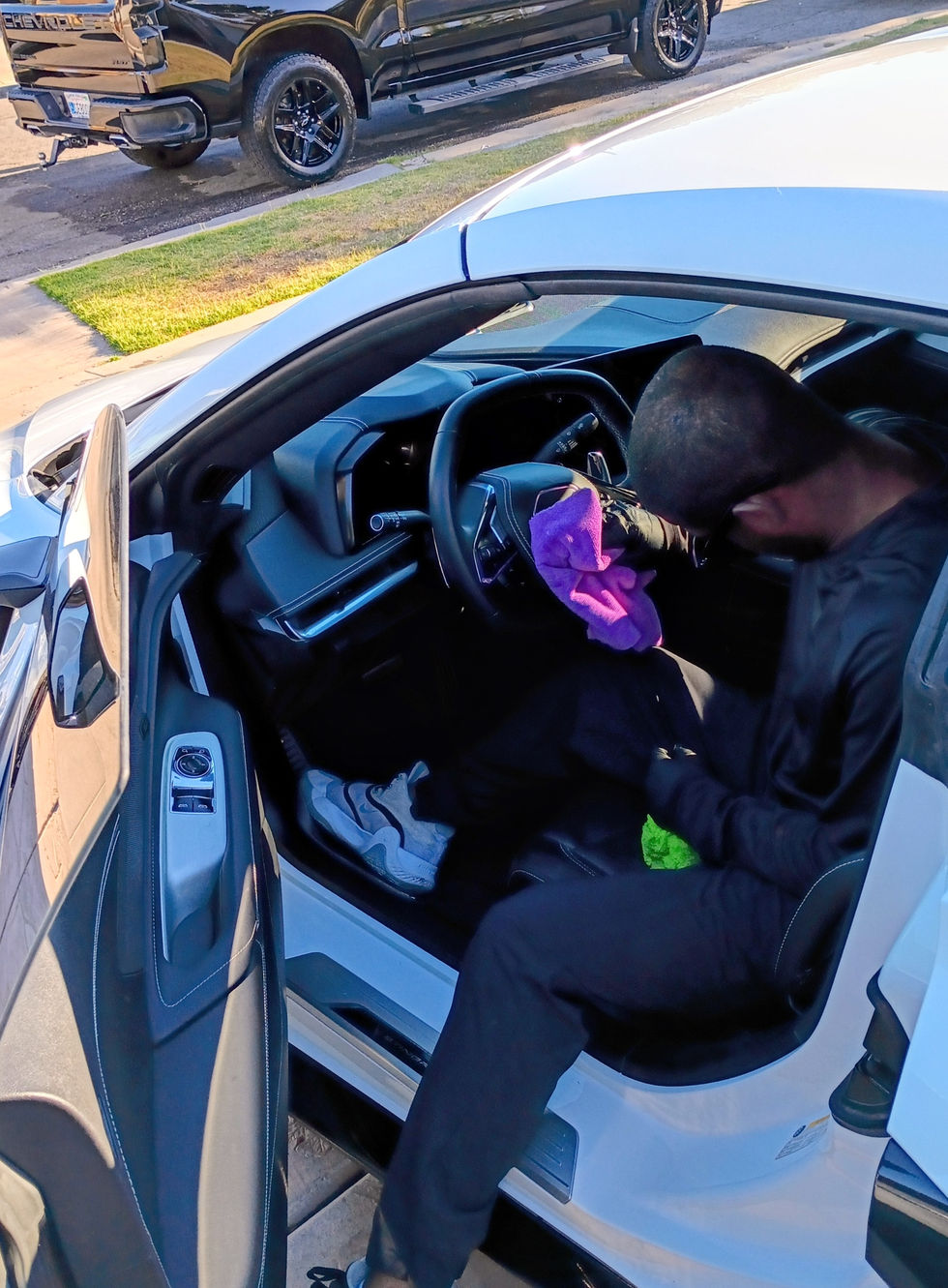 "274 Car Wash on the Spot detailer wiping down the windshield of a white Corvette C8 Stingray with a pink microfiber towel in a residential driveway."