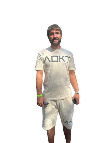 A man wearing a white t-shirt that says AOKT, standing outside. adkt apparel.