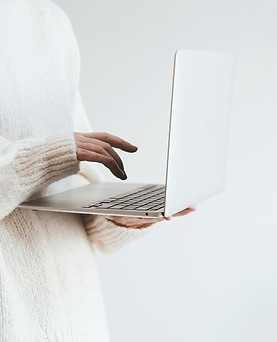 Close up of the arm of a women wearing white sweater writing on a laptop.