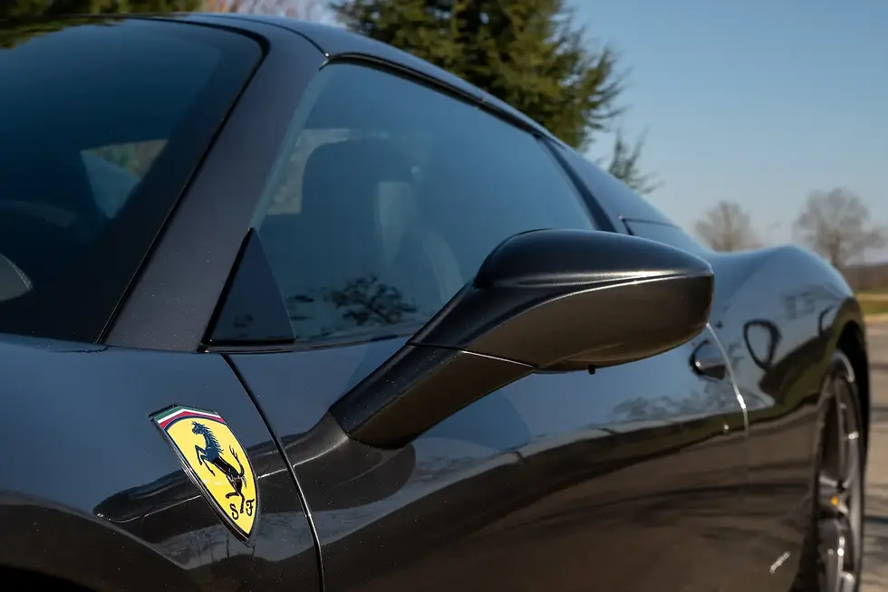 Gros plan d’une Ferrari noire avec logo jaune, rétroviseur brillant, garée dehors sous ciel bleu.