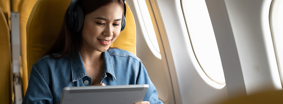 mulher jovem usando um tablet, com fone de ouvido sentada perto da janela no avião