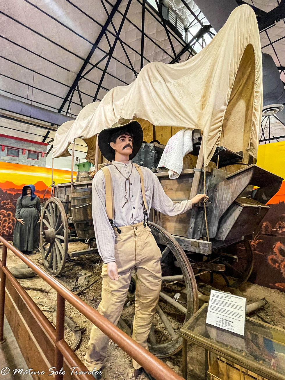 a lifesized replica of a covered wagon carrying all the household goods of a family from the late 1800s. A statue of a pregnant woman and another of a man, possibly her husband, stand next the wagon as they would have walked alongside it.