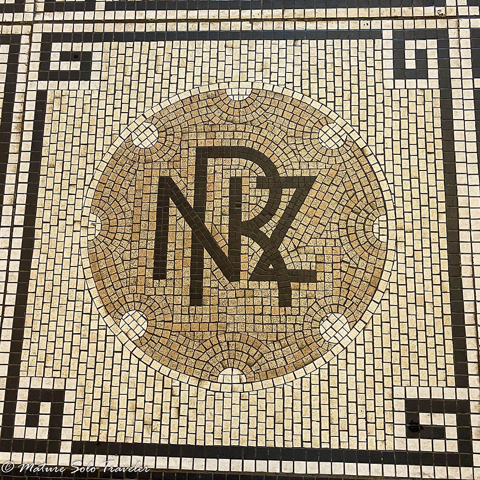 a mosaic on the floor of the dunedin railway station has the initials NRZ in brown tile within a light brown circle. The initials stand for New Zealand Railway. That dark circle is surrounded by tan tiles and they in turn are surrounded by a narrow row on all four sides of the matching brown of the initials in the centre.