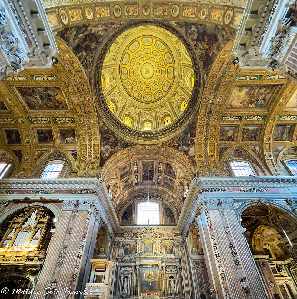 looking up at the ceiling of the church, the dome in the centre of the arched roof has geometric glass designs, the rest of the ceiling is painted alfrescos. The arched windows high in the walls allow matureal light in. The marbled columns surround entry into side chapels. The whole scenario is gods, and creams, magestic colours.