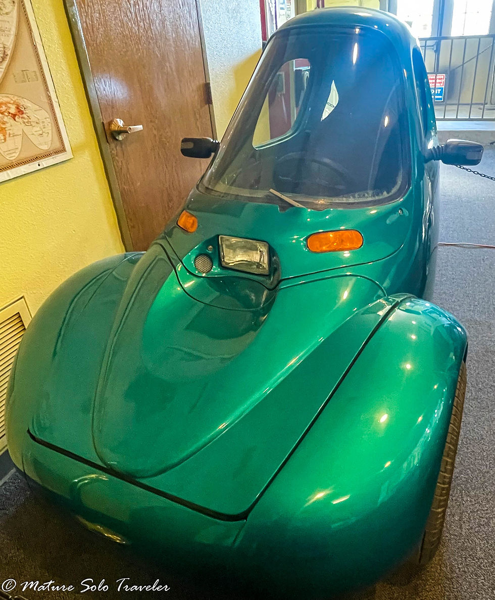 an electric vehicle that looks futuristic. green metallic paint with large front end, it is only wide enough for the driver to sit in.