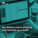 A imagem mostra um notebook aberto com a tela de uma caixa de e-mail. Em primeiro plano, mãos digitam no teclado. Ao lado do computador há uma xícara de café e um par de óculos sobre a mesa