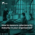 The image depicts a modern corporate environment, with a group of people working in front of computers. In the background, two women are standing and conversing; one of them is holding a clipboard, suggesting a professional meeting or discussion. The space has large arched windows and exposed brick walls, with good natural lighting.