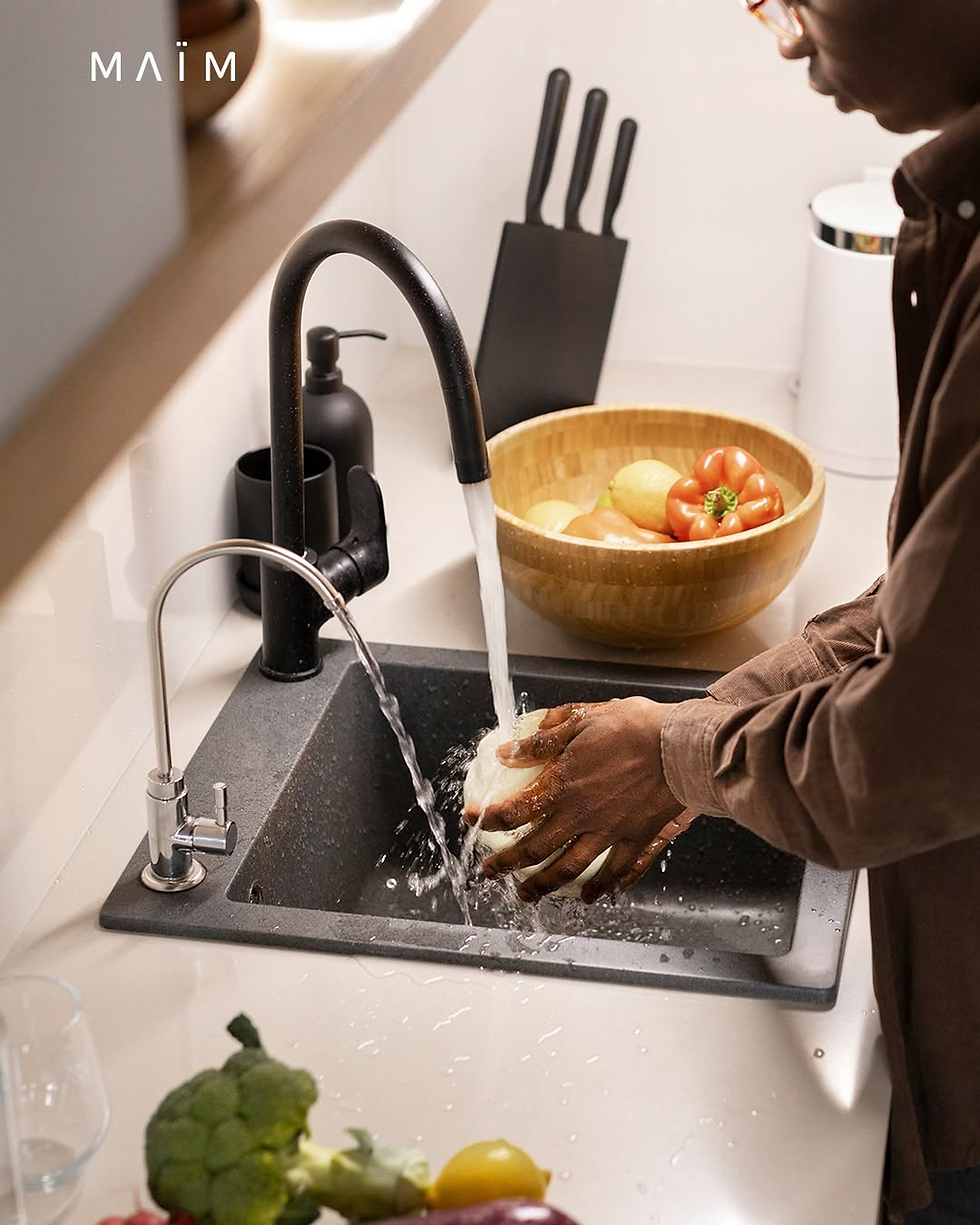 Persona lavando vegetales frescos en el fregadero de su cocina utilizando un purificador de agua para casa MAÏM.