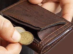 Billetera vegana sostenible hecha de corcho marrón oscuro, que muestra un primer plano de unas manos sacando monedas de un bolsillo con cremallera.