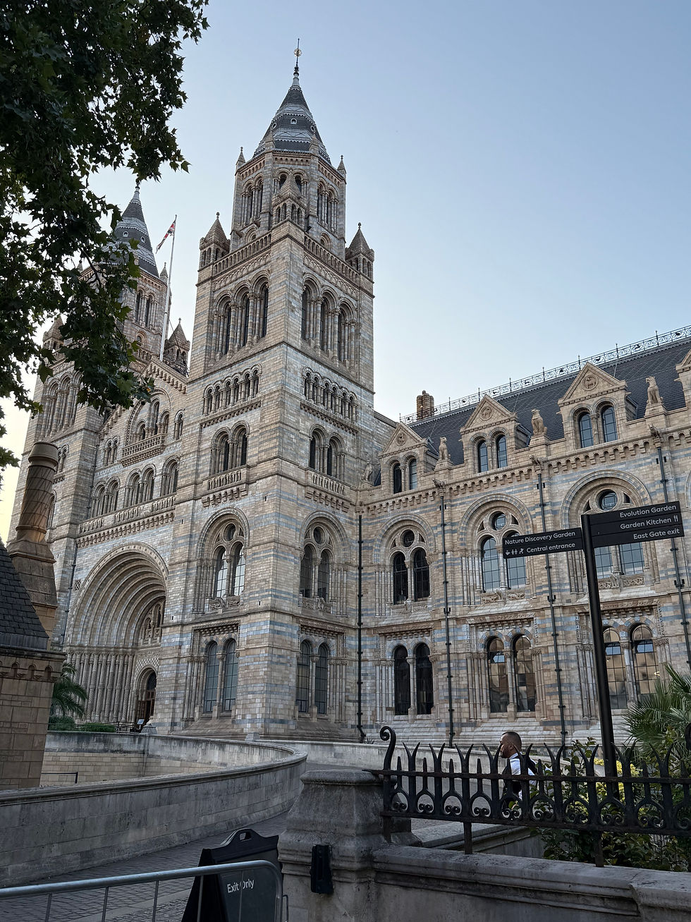 Historic stone building with arched windows and towers; a person walks nearby. Trees frame the scene on a clear day. Sign reads "Exit Only."
