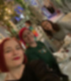 Three women smiling in a decorated cafe with hanging lights and plants. They are seated at a table with tea cups and utensils.