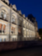 Illuminated historic building facade at night. Arched windows, intricate stonework, deep blue sky. Majestic and calm atmosphere.
