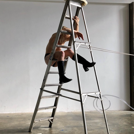 a dancer hangs partially nude from a ladder in hackney, created in the project space as part of fieldworks dance's artist lab