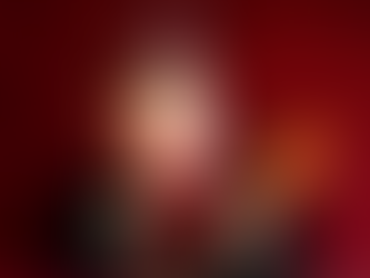 Singing telegram performer in black uniform with red striped necktie and musical note cap, holding ukulele against red backdrop