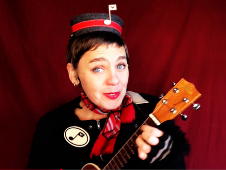 Singing telegram performer in black uniform with red striped necktie and musical note cap, holding ukulele against red backdrop