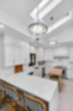 Modern white kitchen with quartz countertops, pendant lights, and skylights