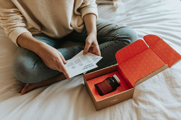 Woman sitting on bed while reading package materials included within the Nouri subscriptio