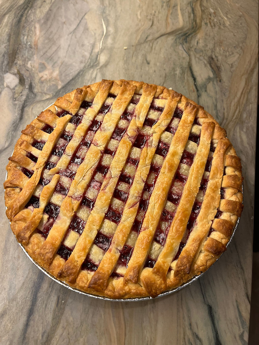Cherry pie with lattice crust on marble countertop, showing golden brown pastry and vibrant red filling.
