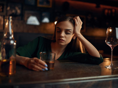 Person sitting alone holding a glass of alcohol and looking unwell