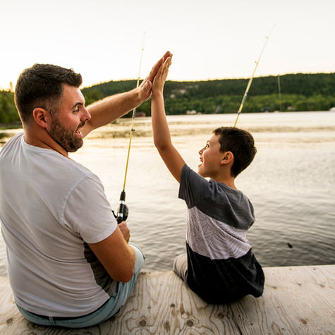 Dad and child fishing together, sharing a high five - capturing trust, presence and quiet connection.