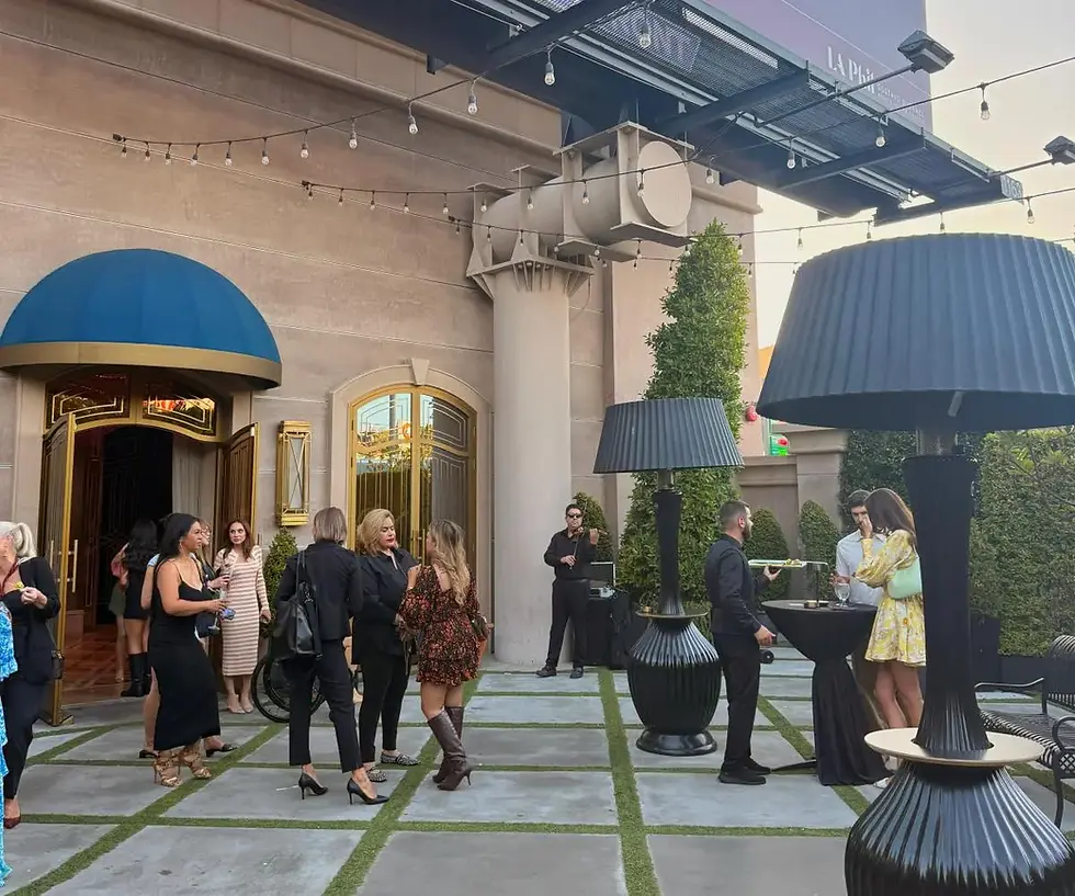 Guests gather outside a building with a blue awning and open golden doors.