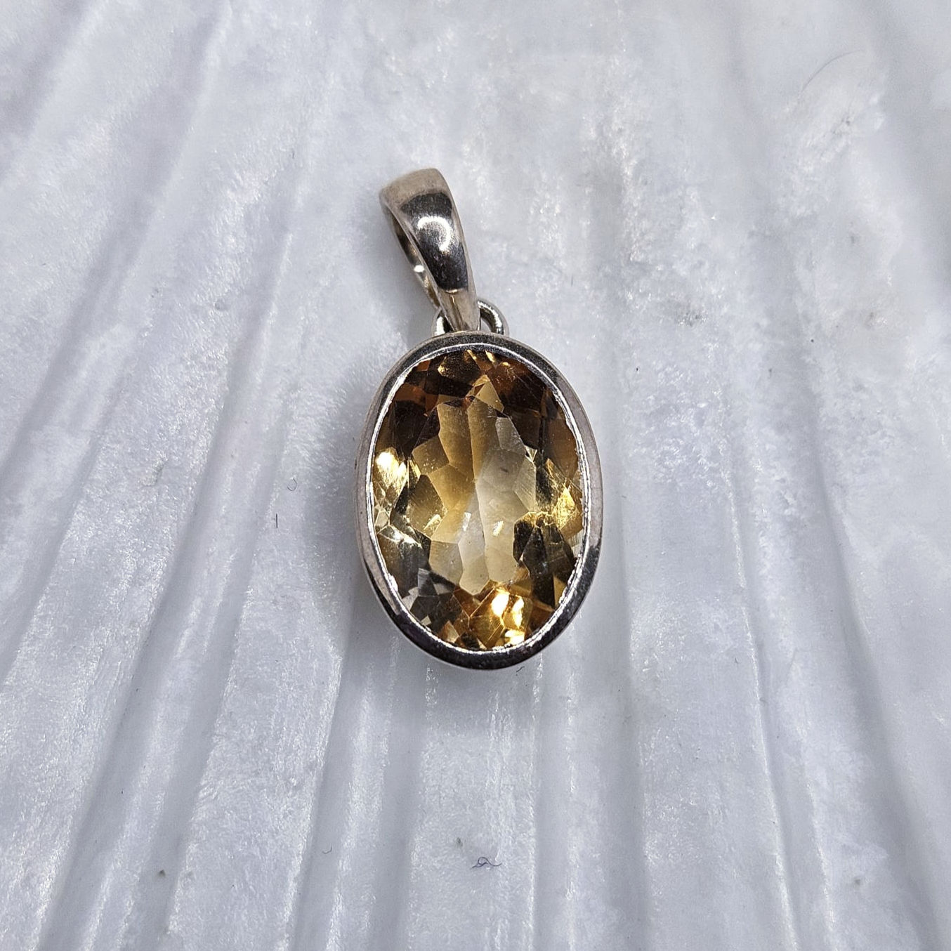 Oval faceted citrine bezel-set in a sterling silver pendant setting
