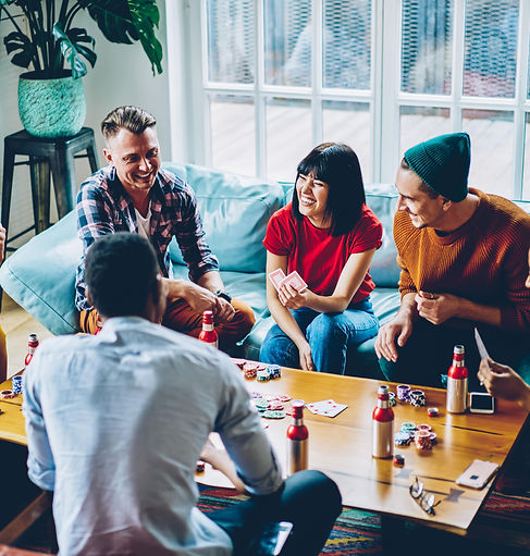 A group of young people playing cards and using chips around a coffee table in a living room, laughing and enjoying their time together.