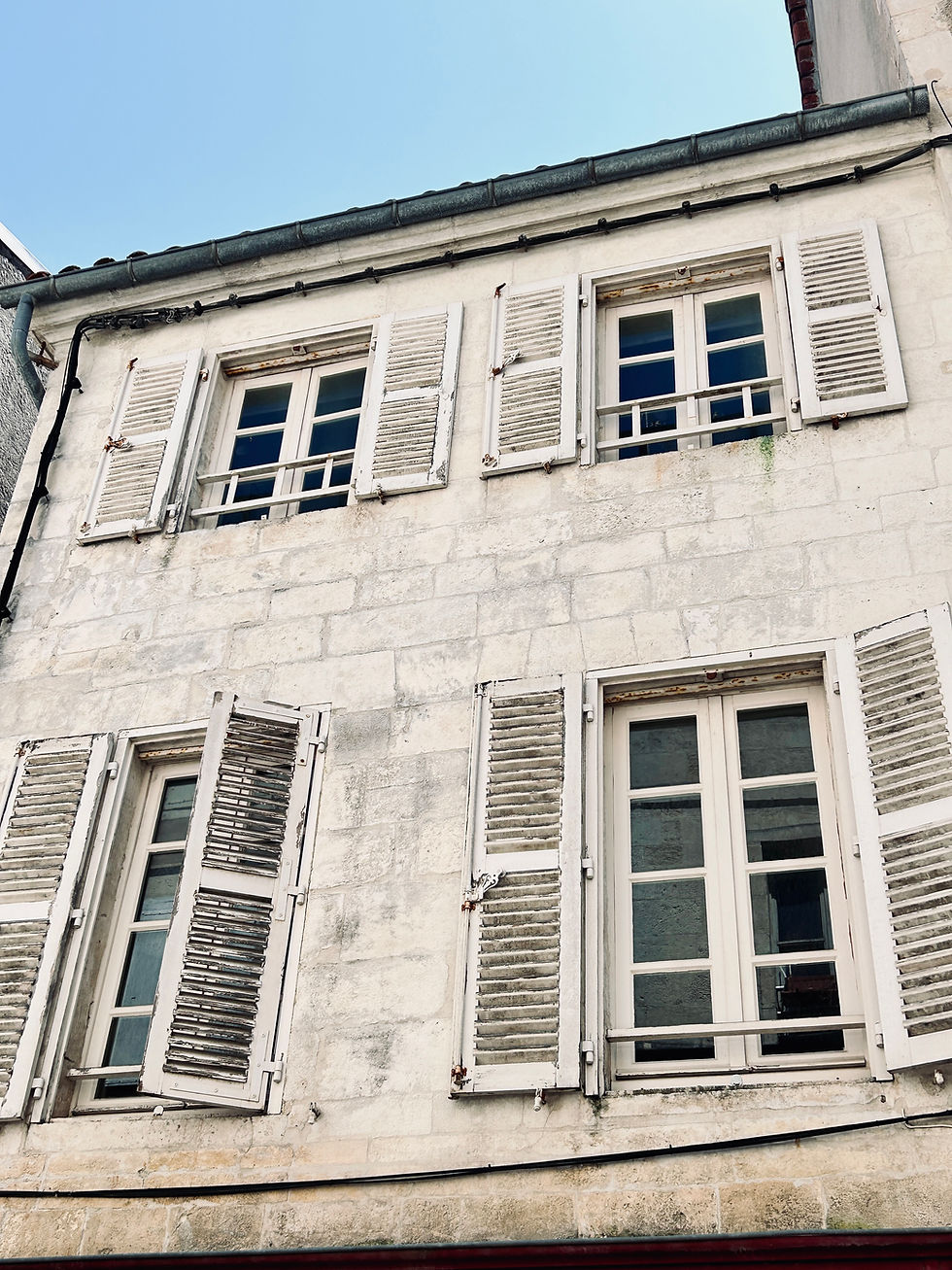 Stone building facade with six windows, white shutters, and weathered appearance. Clear blue sky above. Mood is calm and historical.
