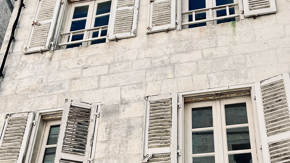 Stone building facade with six windows, white shutters, and weathered appearance. Clear blue sky above. Mood is calm and historical.