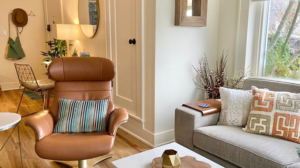 MidMod Style + Super Walkable + Heart of Fremont bed and breakfast. Cozy living room with a brown leather chair, striped pillow, gray sofa, and patterned cushions. White walls, mirror, and wooden decor.