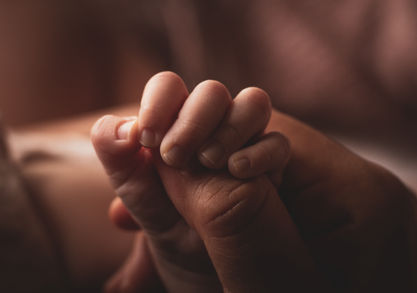 Newborn baby holding mother's finger