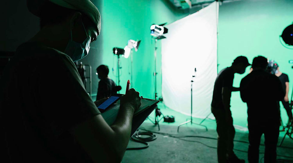 A Production Avenue crew member taking notes on a clipboard while silhouetted against a lit green screen studio setup during a video production in Hong Kong.