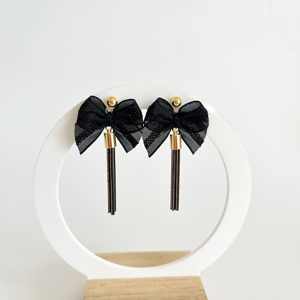 Paire de boucles d'oreilles pendantes pompon noir et or accrochées sur un support circulaire blanc.