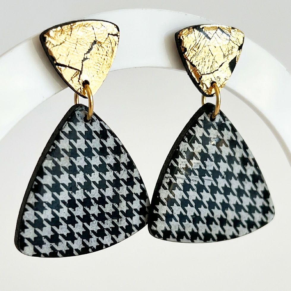 Vue rapprochée des boucles d'oreilles pied-de-poule et puces en feuille d'or posées à plat.