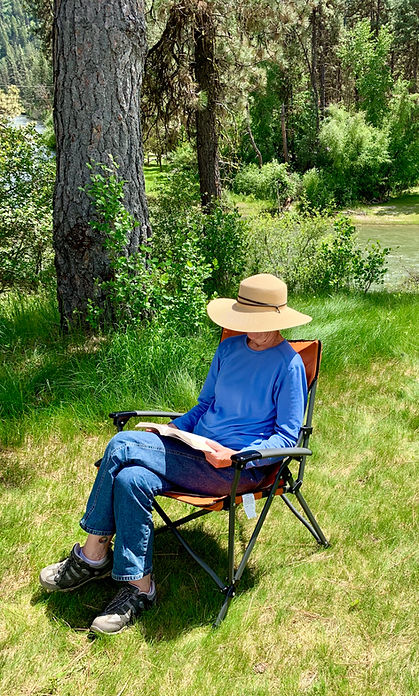 Author, Laurie Buchanan, sitting in a chair by a river reading a book